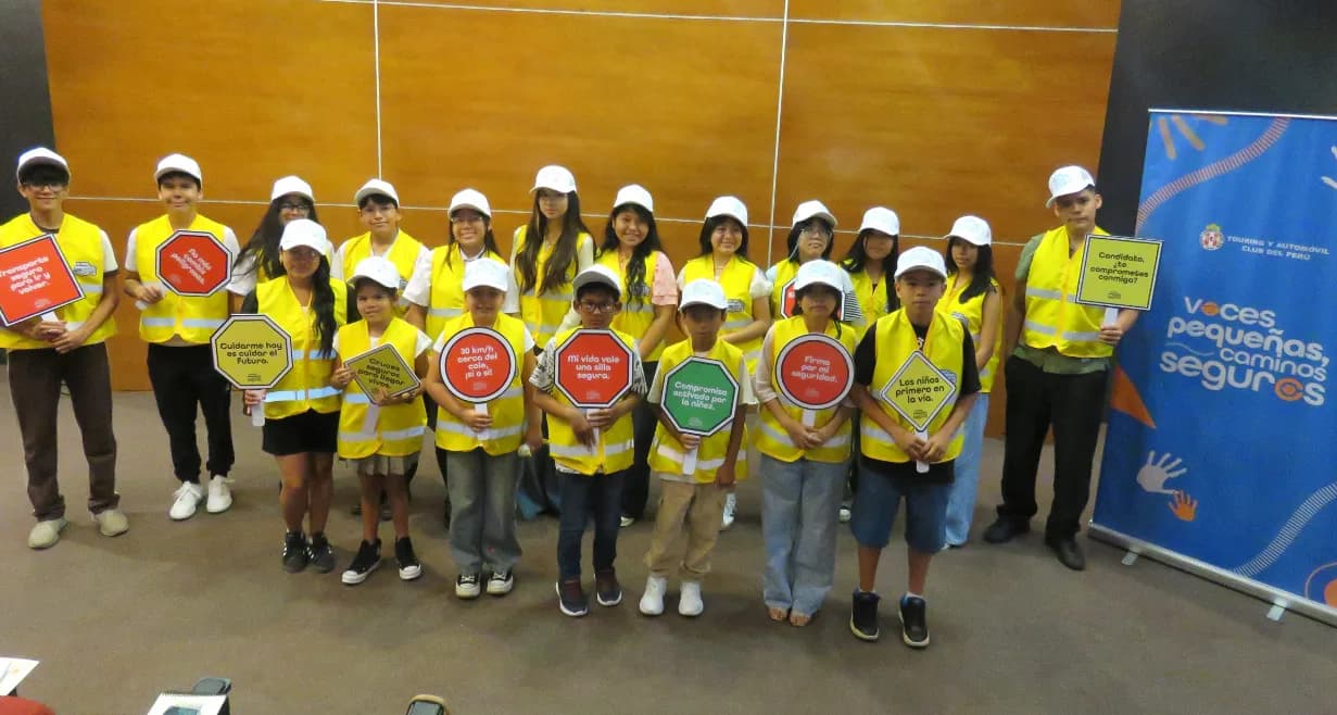 Niños y adolescentes con chalecos reflectantes y carteles de seguridad vial junto al banner de Touring